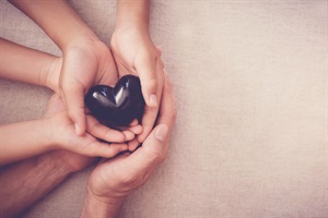 Several hands cradling a black heart